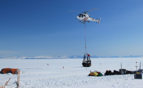 Sling load containing the snowmobile is lowered by the helicopter.