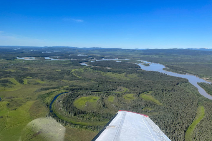 A view of airplane wing over Alaska forest and river